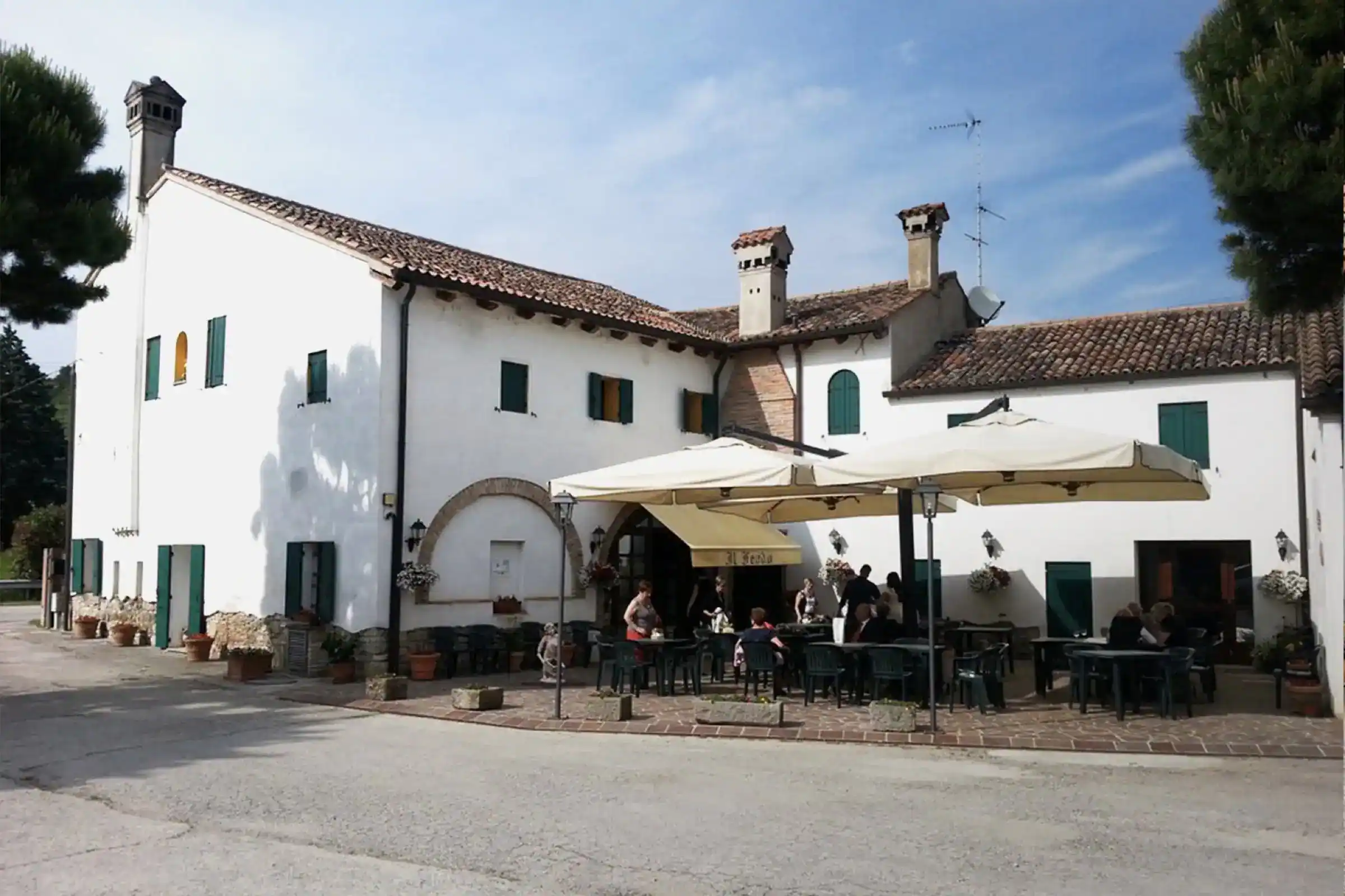 Il casale dell'Agriturismo Il Feudo visto dal cortile, con ospiti seduti sotto gli ombrelloni