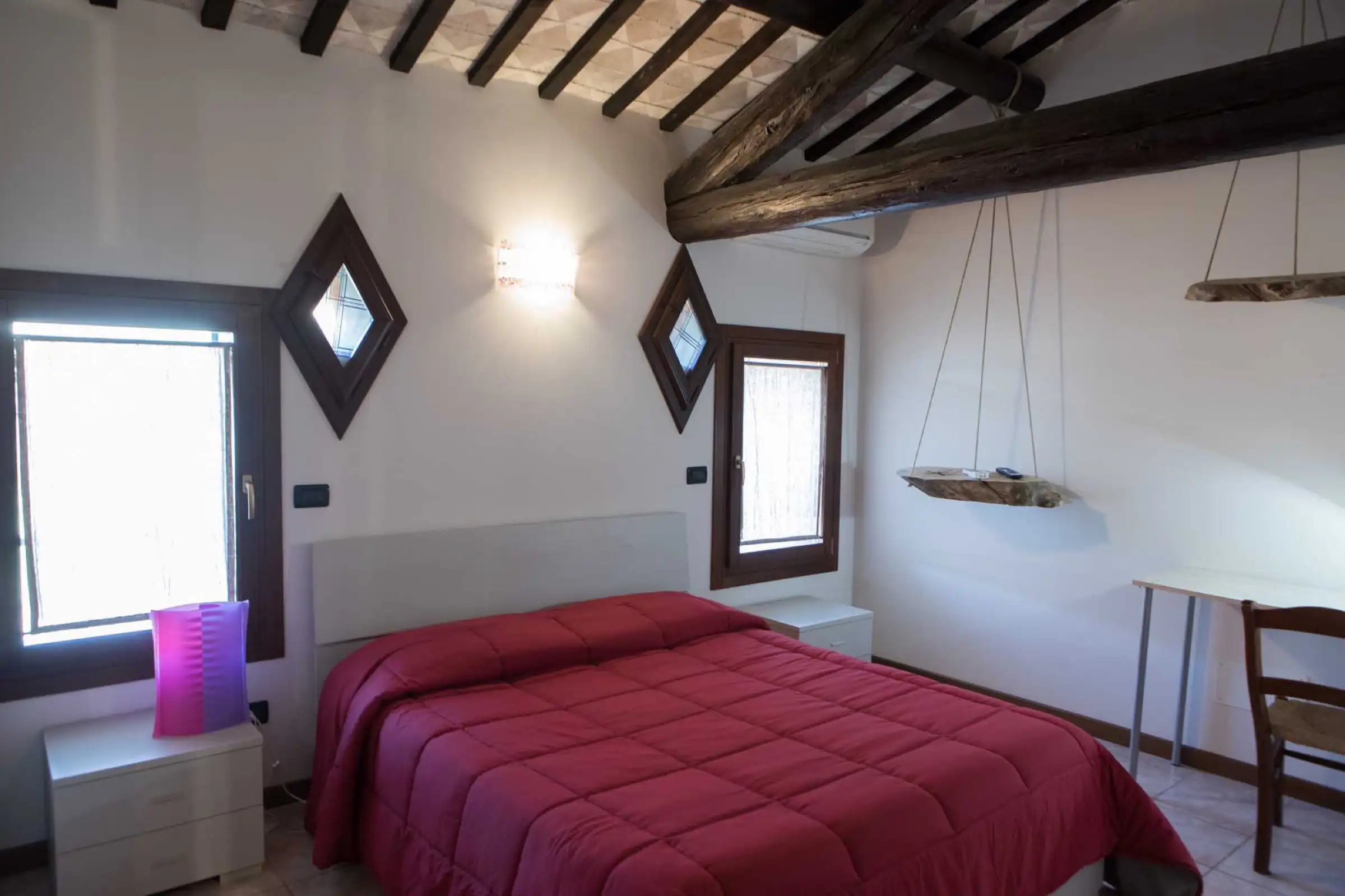 Dachzimmer mit Holzbalken, Doppelbett und rautenförmigen Fenstern