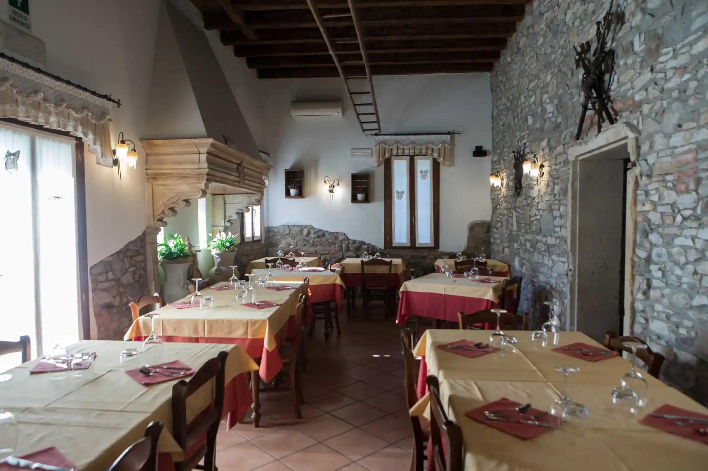 Der Speisesaal des Restaurants mit Natursteinwänden, Holzbalken und gedeckten Tischen